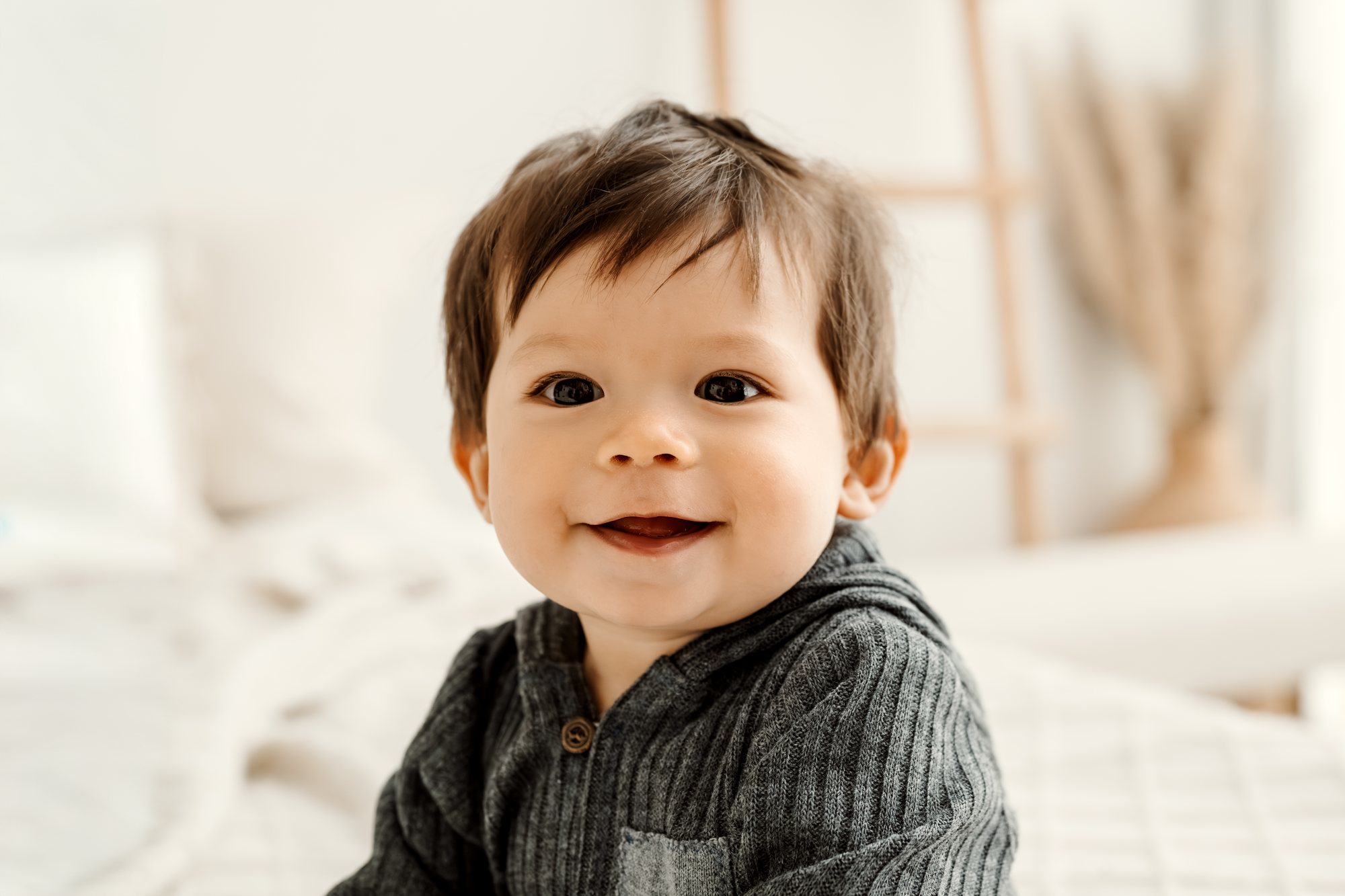 Baby im Strickpullover sitzt auf dem Bett